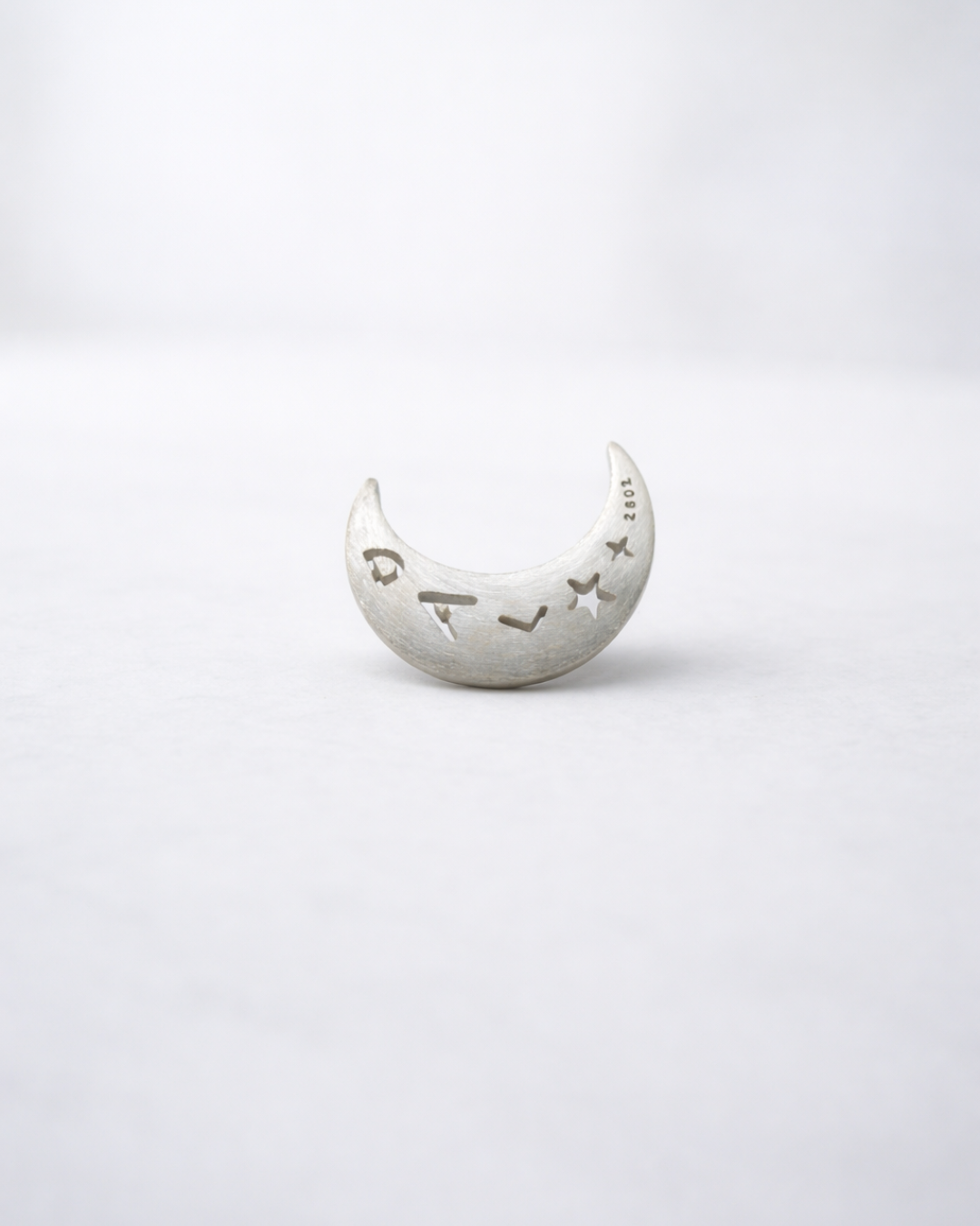 Silver moon-shaped object with engraved text on a white background